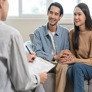 Smiling couple holds hands while consulting with a lawyer or counselor about family matters.