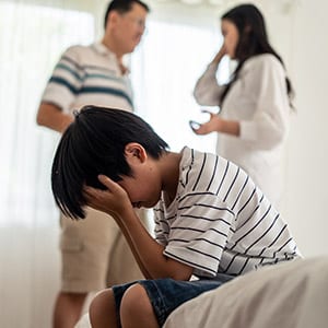 Child distressed, face in hands; two adults argue in background. Symbolizes divorce's impact.