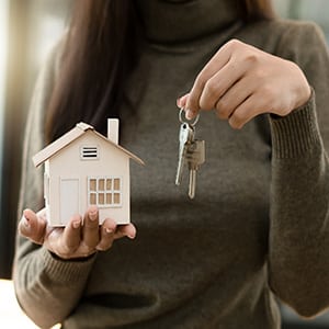 Woman holding house model and keys for Texas divorce and family home asset division
